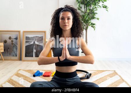 Femme aux cheveux bouclés avec les mains jointes faisant de l'exercice de relaxation à accueil Banque D'Images