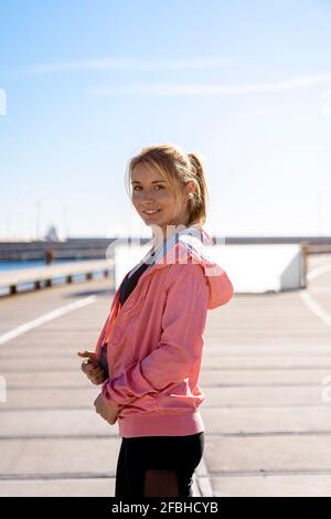 Jeune femme souriante debout sur la promenade pendant la journée ensoleillée Banque D'Images