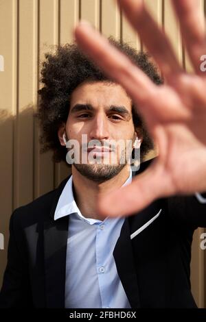 Afro homme montrant la main tout en se tenant au mur doré Banque D'Images