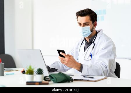 Un médecin portant un masque de protection avec un smartphone assis au bureau de l'hôpital Banque D'Images