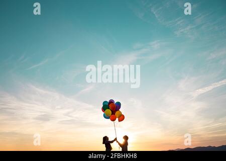 Filles en silhouette jouant avec des ballons multicolores pendant le coucher du soleil Banque D'Images