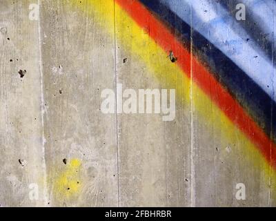 Jaune, rouge, bleu, blanc et noir pulvérisés en bandes diagonales sur un mur en béton gris Banque D'Images