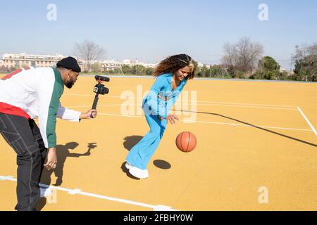Un homme filmant une amie féminine jouant au basket-ball sur un terrain de sport Banque D'Images