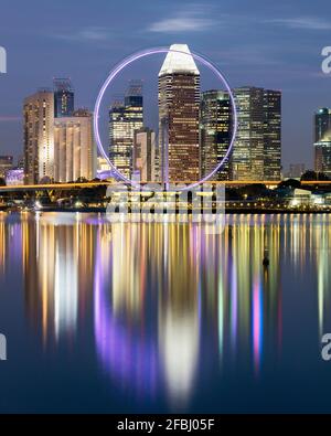 Singapour, longue exposition de Marina Bay au crépuscule avec Singapore Flyer et gratte-ciels du centre-ville en arrière-plan Banque D'Images