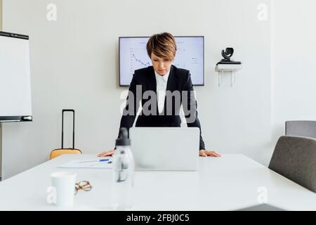 Femme d'affaires sérieuse regardant un ordinateur portable tout en se penchant sur le bureau contre écran de projection au bureau Banque D'Images