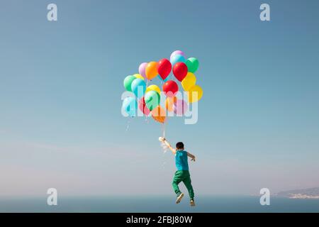 Garçon volant avec un tas de ballons dans le ciel Banque D'Images