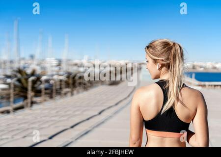 Athlète féminine avec casque intra-auriculaire qui regarde loin tout en restant debout promenade en journée ensoleillée Banque D'Images