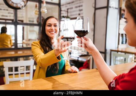 Des amies joyeuses qui toastent des verres de vin à la table bar Banque D'Images