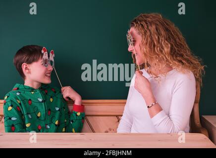 Mère et fils souriants regardant à travers les accessoires de Noël à la maison Banque D'Images