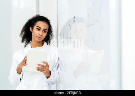 Femme chercheuse confiante tenant une tablette numérique tout en s'appuyant sur un tableau blanc en laboratoire Banque D'Images