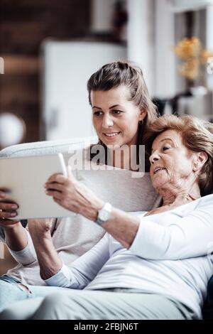 Femme âgée utilisant une tablette numérique tout en se relaxant par la petite-fille à accueil Banque D'Images