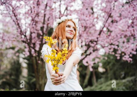 Jeune femme tenant un bouquet de fleurs jaunes debout devant d'amandiers tout en regardant loin Banque D'Images