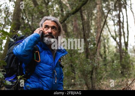 Homme senior parlant sur smartphone tout en explorant la forêt Banque D'Images