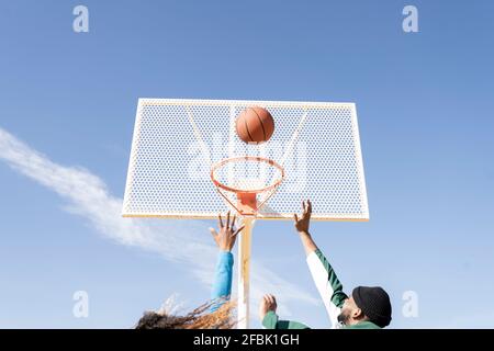 Des amis masculins et féminins jouant au basket-ball par beau temps Banque D'Images