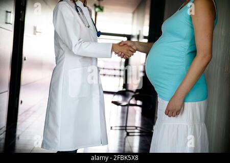 Femme médecin se secouant les mains avec la femme enceinte après examen à hôpital Banque D'Images