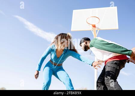 Femme souriante jouant au basket-ball avec un ami masculin sur le terrain Banque D'Images