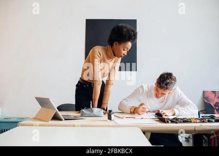 Jeune femme regardant l'homme écrire avec un stylo de fontaine pendant assis à une table dans le studio Banque D'Images