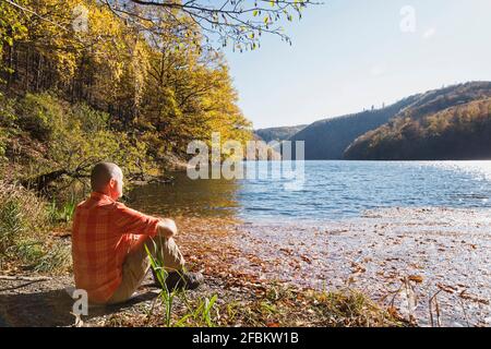 Homme senior se détendant sur les rives du réservoir de Rursee en automne Banque D'Images