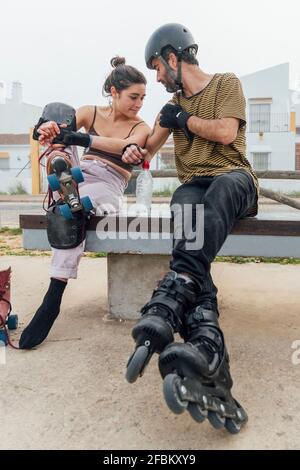 Jeune femme regardant le tatouage de l'homme en étant assise sur le banc avec patins à roulettes Banque D'Images