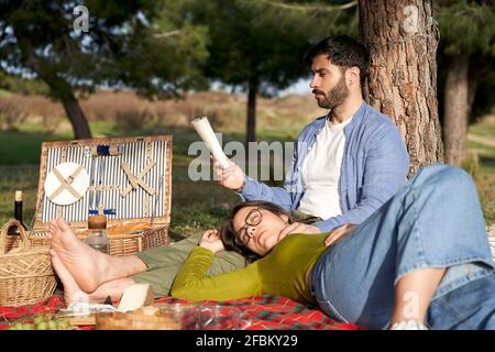 Femme se détendant pendant que l'ami lit le livre sur la couverture pendant le pique-nique Banque D'Images