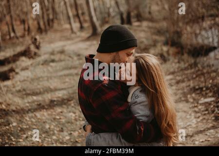 Femme en denim veste embrassant hipster petit ami en forêt pendant l'automne Banque D'Images