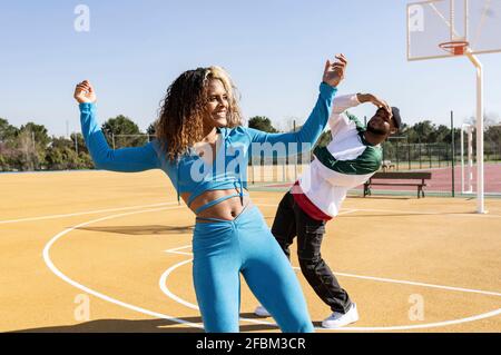 Femme souriante dansant avec un ami sur le terrain de basket-ball Banque D'Images