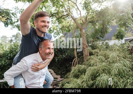 Père donnant une promenade en pigeyback à un fils joyeux dans l'arrière-cour Banque D'Images