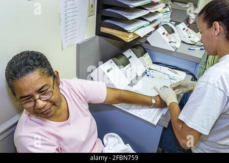 Miami Beach Florida, centre de santé communautaire, femme hispanique femmes test de cholestérol gratuit regarde loin, le sang de prélèvement technicien Banque D'Images