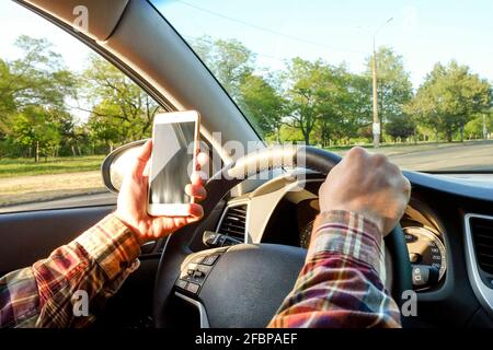 Gros plan sur les mains d'un jeune homme tenant le volant de la voiture. Panneau de tableau de bord, support de téléphone. Homme d'affaires conducteur, intérieur du véhicule, coucher de soleil Banque D'Images