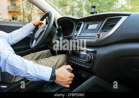 Gros plan d'un jeune homme qui conduit une voiture chère, ceinture de sécurité bouclée, mains avec attention sur le volant et changement de vitesse, clés dans le contact. Bus Banque D'Images