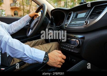 Gros plan d'un jeune homme qui conduit une voiture chère, ceinture de sécurité bouclée, mains avec attention sur le volant et changement de vitesse, clés dans le contact. Bus Banque D'Images