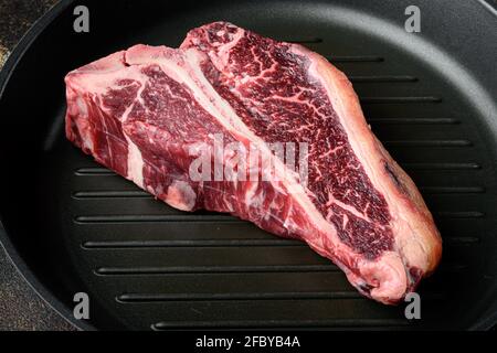 Set de steak de bœuf marbré, sec et vieux, dans une poêle en fonte, sur fond rustique foncé Banque D'Images