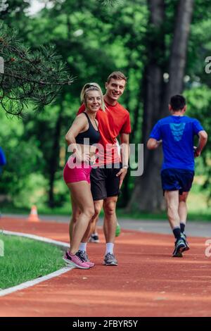 Un jeune couple s'étire avant de commencer sa routine de jogging matinale sur une piste de tartan au parc. Banque D'Images