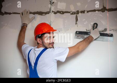 travaux sur la finition des murs avec des mélanges de plâtre et de mastic lors de la construction d'une maison. ouvrier de construction plâtrage façade de bâtiment de haute hauteur avec couteau à mastic. nivellement murs en pierre Banque D'Images