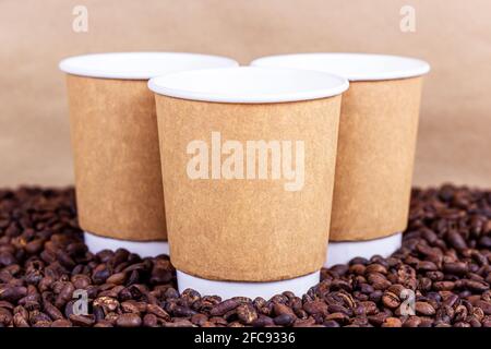 Tasses jetables en carton brun avec café et grains de café torréfiés sur la table avec espace de copie sur fond clair. Concept de plats à emporter. Banque D'Images