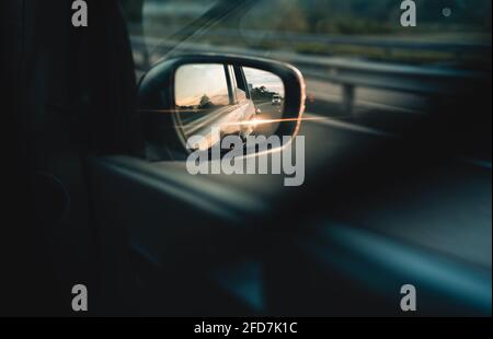 Rétroviseur extérieur et lumière du soleil du soir depuis la carrosserie de la voiture et lueur sur l'autoroute. Concept automobile à mouvement rapide. Vue sur le rétroviseur extérieur Banque D'Images