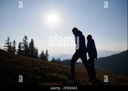 Silhouettes de couple amoureux tenant les mains grimper sur la colline de montagne, regardant le paysage environnant par beau temps ensoleillé. Journée de randonnée active dans les montagnes. Banque D'Images