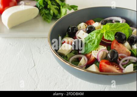 Salade grecque. Salade de légumes frais avec concombres, tomates, olives, oignons, poivrons, feta, laitue et herbes, assaisonnées de sel, poivre et Banque D'Images