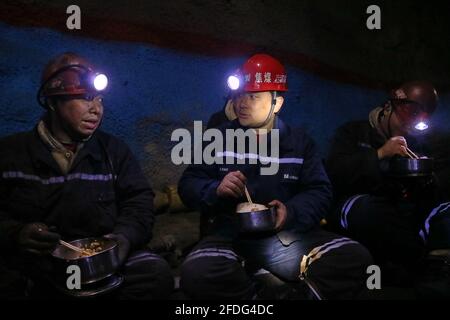 (210424) -- TAIYUAN, 24 avril 2021 (Xinhua) -- Zhang Shiqi (C) a déjeuné avec ses collègues dans un tunnel minier à la mine du'erping du groupe de charbon Shanxi Coking dans la province de Shanxi, dans le nord de la Chine, le 18 mars 2021. Zhang Lianggui, son fils Zhang Hai et son petit-fils Zhang Shiqi avaient tous travaillé comme mineurs de charbon. L'histoire de cette famille de mineurs de charbon sur trois générations illustre l'essor de l'industrie minière chinoise, de l'activité humaine à celle de la technologie. Près de 90 ans, Zhang Lianggui est un mineur à charbon à la retraite. Recruté en 1954, il rappelle les conditions de travail difficiles de l'IM charbon Banque D'Images