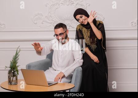 Le couple musulman en vêtements nationaux communique par communication vidéo. Vidéoconférence avec des amis Banque D'Images