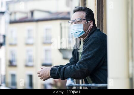 covid-19 verrouillage et peur - triste et déprimé homme mature 65 - 70 ans dans le masque de protection contre les virus à le balcon de la maison avait une vue à l'écart Banque D'Images