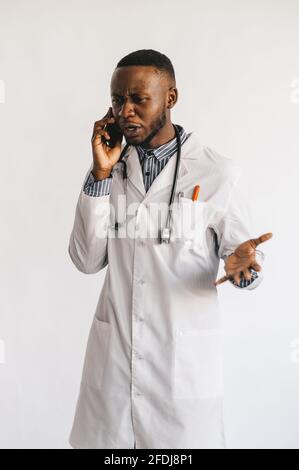 Un médecin afro-américain sérieux et déroutant parlant au téléphone. Le médecin a reçu de mauvaises nouvelles en attente en espérant un résultat positif. Arrière-plan blanc Banque D'Images