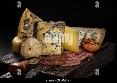 Assortiment de fromages gastronomiques et de saucisses fumées crues sur une planche de bois sur fond sombre. Différents types de fromage : dur et doux avec moule. EXC Banque D'Images
