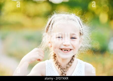 Fille drôle avec cheveux plaits. Enfant exprimant ses émotions. Gros plan portrait de belle blonde joyeuse fille caucasienne souriante démontrant les dents blanches wi Banque D'Images