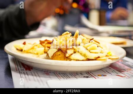 Un patron travaille sur son assiette de petit déjeuner, y compris une grande partie de pommes de terre américaines ou de petit déjeuner. Le reste du repas est flou en arrière-plan. Banque D'Images