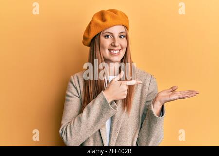 Jeune femme irlandaise portant un look français avec un béret émerveillé et souriant à la caméra tout en présentant avec la main et en pointant avec le doigt. Banque D'Images