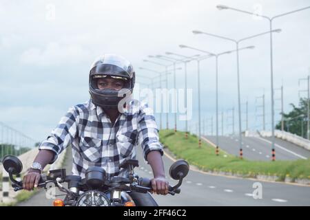 Un motard africain dans le casque, à bord d'une moto, passe autoroute Banque D'Images