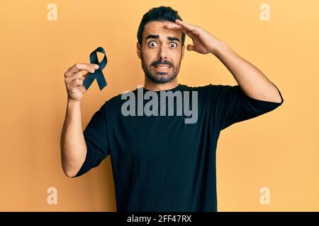 Jeune hispanique tenant un ruban noir stressé et frustré avec la main sur la tête, surpris et fâché visage Banque D'Images