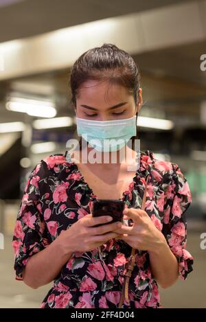 Femme portant un masque facial pour la protection contre le coronavirus Covid-19 à l'extérieur la nuit, lorsque vous envoyez des sms avec votre téléphone Banque D'Images