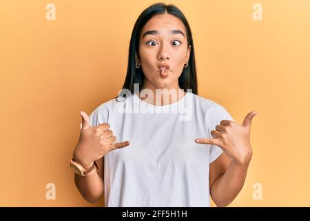 Jeune femme asiatique faisant le signe de shaka avec les mains faisant le visage de poisson avec la bouche et les yeux de bourdonner, fou et comique. Banque D'Images